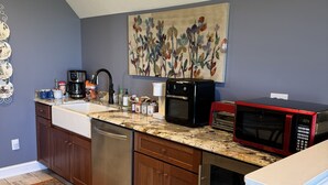 A kitchen with dark gray walls, a marble countertop, and wooden cabinets. There is a painting of flowers on the wall, a coffee maker, a microwave, and a dishwasher.