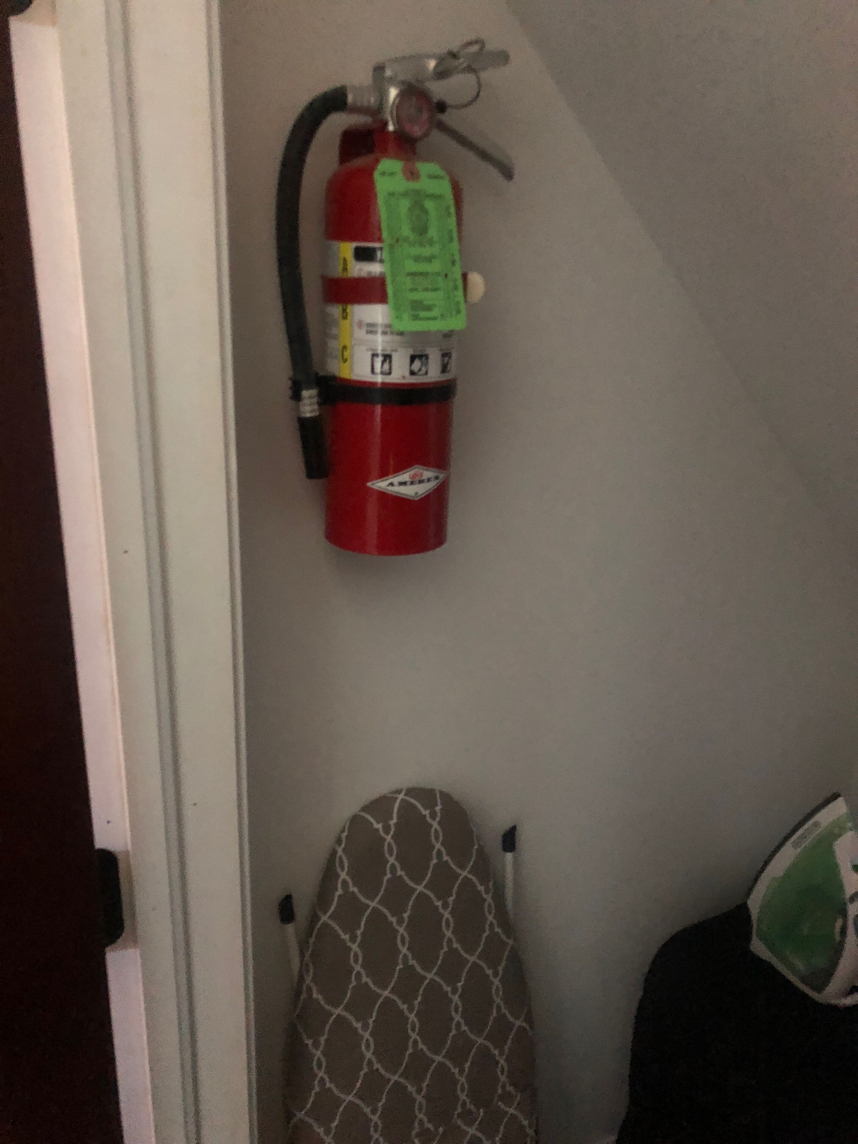 A red fire extinguisher mounted on a wall, a patterned chair, and a backpack on the floor.