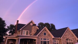 A house with a stone facade and a prominent chimney, under a sky with a visible rainbow.