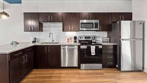 A modern kitchen with dark wooden cabinets, stainless steel appliances, and a granite countertop. - Studio King Suite with Kitchen | 304 (Asheville)
