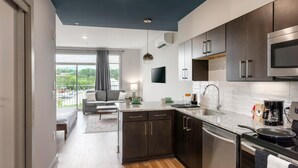 A modern kitchen with dark cabinets, a stainless steel microwave, and a built-in dishwasher. - Studio King Suite with Kitchen | 304 (Asheville)
