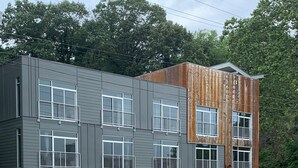 A modern multi-story building with a grey facade, multiple balconies, and a wooden accent wall. - Studio King Suite with Kitchen | 304 (Asheville)