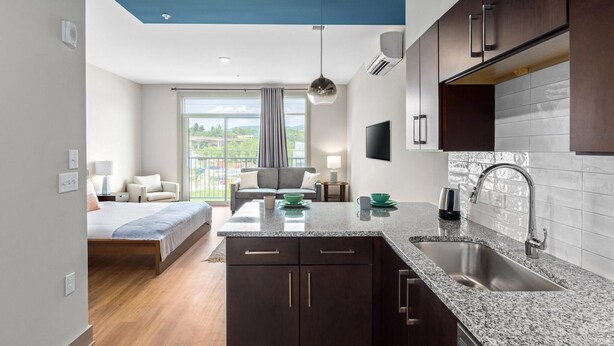 A modern hotel room with a kitchen area, a balcony with a view, and a large bed. - Studio King Suite with Kitchen | 304 (Asheville)