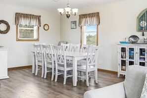 A dining area with a white table and chairs, a chandelier, and a cabinet with books. - Six Pack | 1169 ft from the beach | Dog Friendly, Private Pool, Hot Tub | Nags Head (Nags Head)