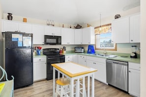 Una cocina compacta con armarios blancos, un refrigerador negro, microondas, tostadora y lavavajillas.