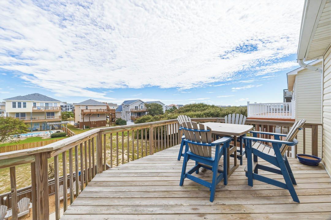 A wooden deck with outdoor furniture, a view of neighboring houses, and a clear sky.