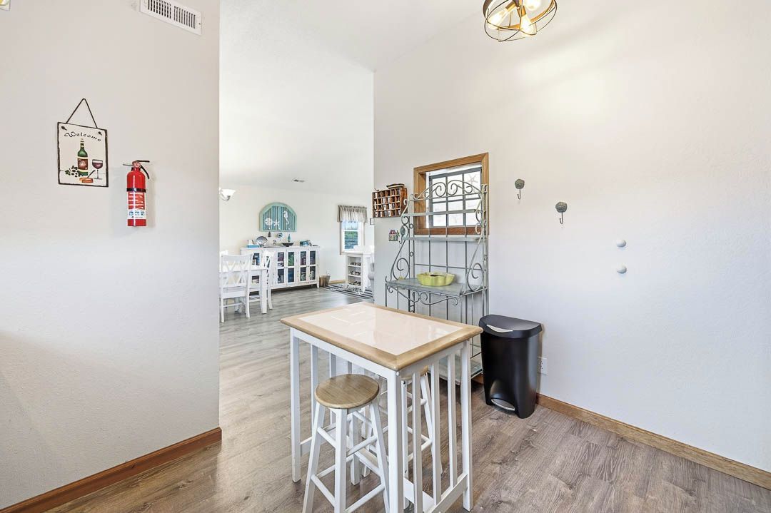 A kitchen with a white table, stools, a black trash bin, and a fire extinguisher on the wall.