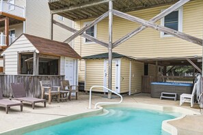 A swimming pool with a wooden deck, lounge chairs, and a hot tub in a residential setting.