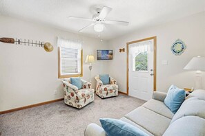 A living room with a ceiling fan, two armchairs, a sofa, and a door leading to a balcony.