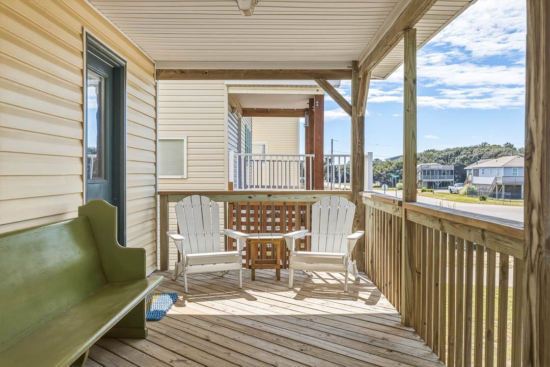 A wooden deck with a bench and Adirondack chairs, a small table, and a view of the surrounding area.