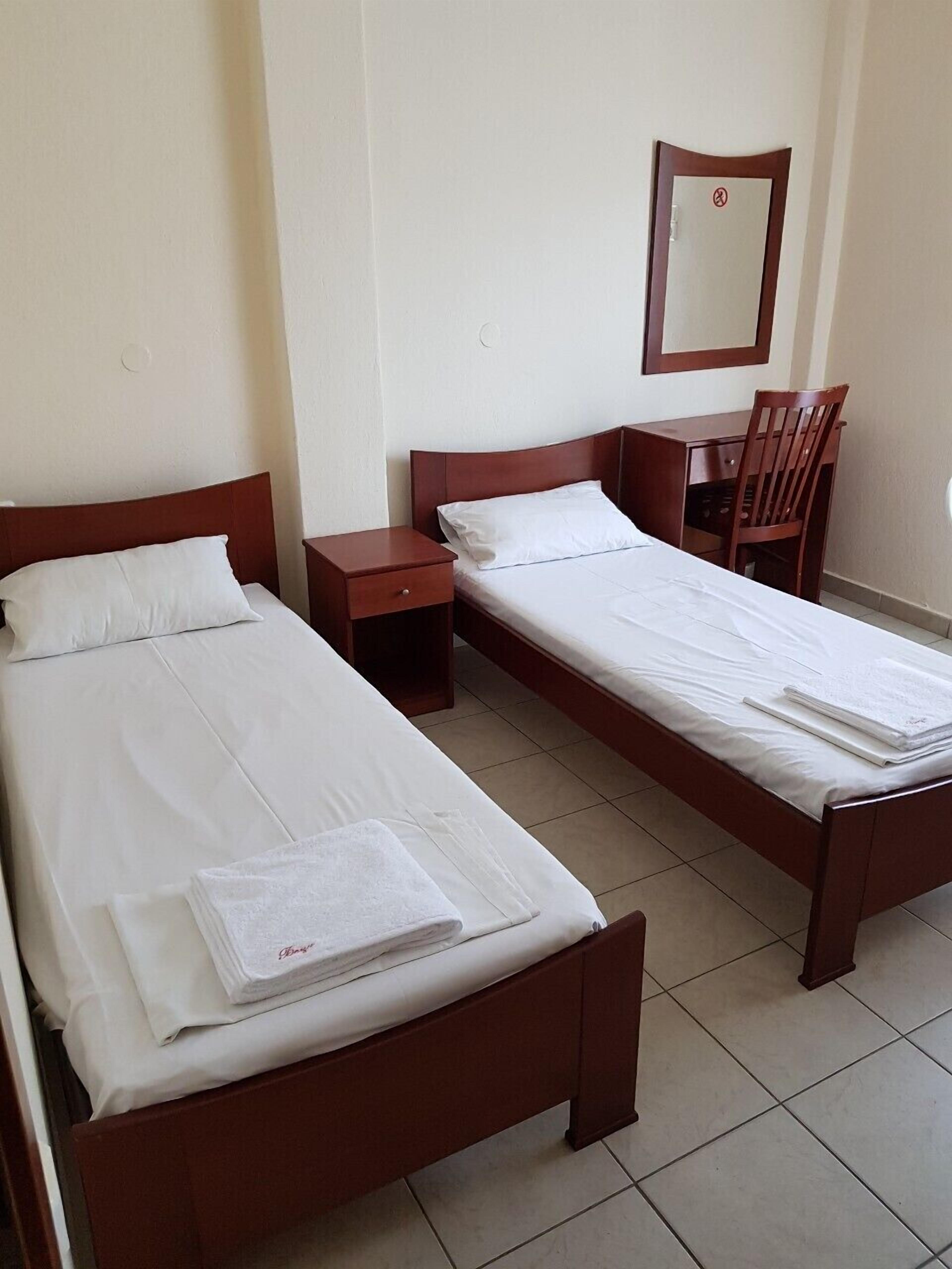 A hotel room with two single beds, a wooden desk, a chair, and a small bedside table.