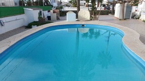 A clear blue swimming pool with a curved edge, surrounded by a paved area and some greenery.