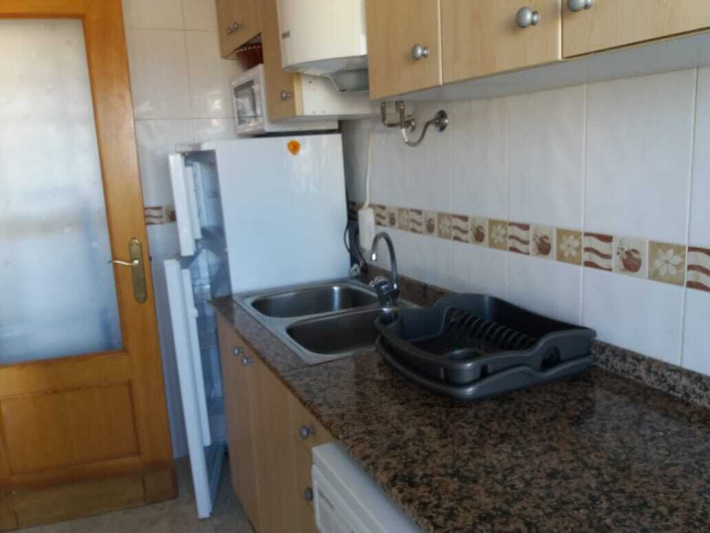 A kitchen with granite countertops, a sink, a dish rack, and wooden cabinets.