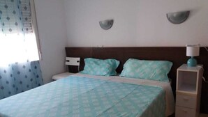 A bedroom with a bed, two wall-mounted lamps, a bedside table, and a window with curtains.
