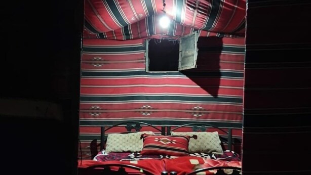 A small, dimly lit room with a single bed, striped curtains, and a small window. - Um Al Tawaqi (Wadi Rum)