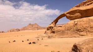 A desert landscape with a prominent rock formation arching over the sand. - Um Al Tawaqi (Wadi Rum)