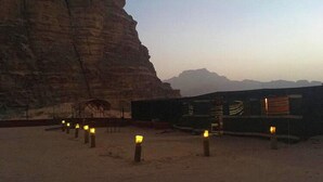 A desert landscape with a large rock formation and a building with a flat roof. - Um Al Tawaqi (Wadi Rum)