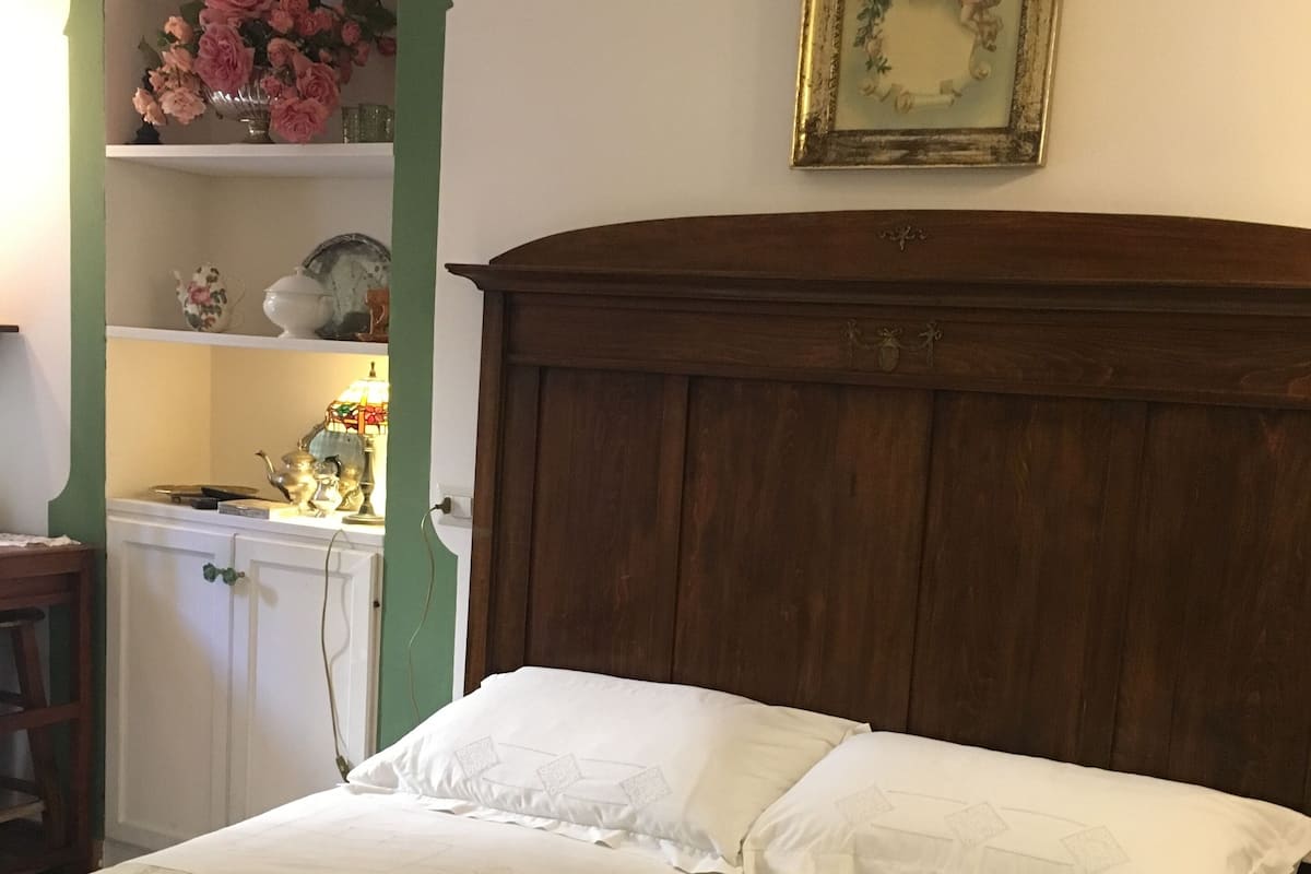 Une chambre à coucher avec une tête de lit en bois, une couvre-lit à motifs floraux et une étagère verte ornée d’objets décoratifs.