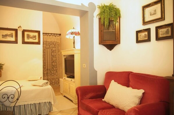 Una sala de estar acogedora con un sofá rojo, una mesita con mantel blanco, un televisor y cuadros en la pared.