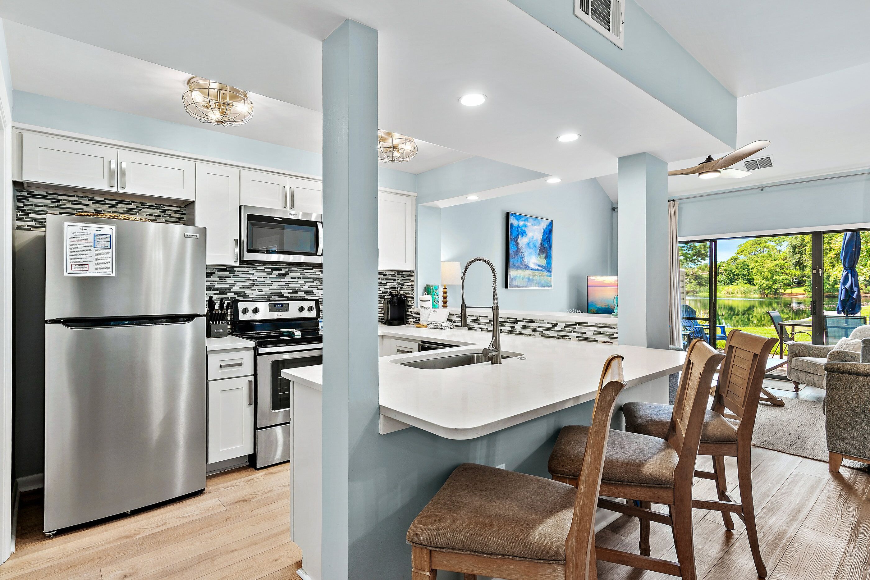 A modern kitchen with stainless steel appliances, a central island with bar stools, and a view of a lake through large windows.