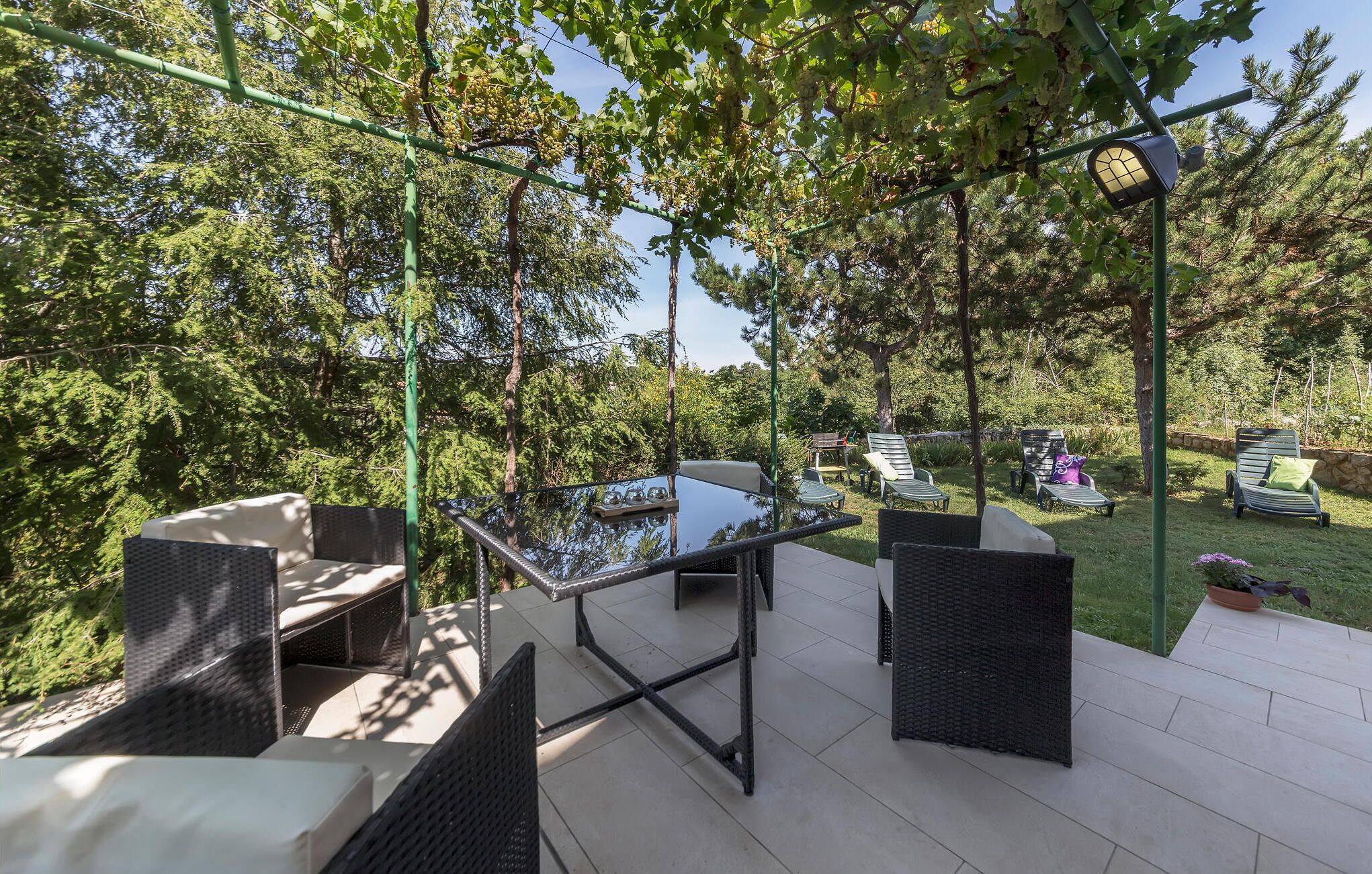 Un patio exterior con mobiliario de mimbre, una mesa con cubierta de vidrio y una pérgola cubierta de hiedra.