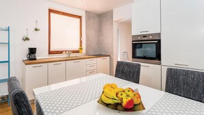 Een moderne keuken met witte kasten, een inbouwoven en een eettafel met een fruitige decoratie.