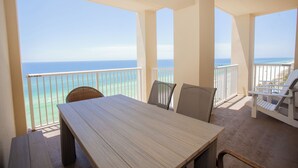 A balcony with a wooden table and chairs, overlooking a beach and the ocean. - Grand Panama Resort Direct Beachfront 3 Bed with Bunks and Amazing Views (Panama City Beach)