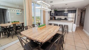 A modern kitchen with dark cabinets, a stainless steel refrigerator, and a dining area with a wooden table and chairs. - Grand Panama Resort Direct Beachfront 3 Bed with Bunks and Amazing Views (Panama City Beach)