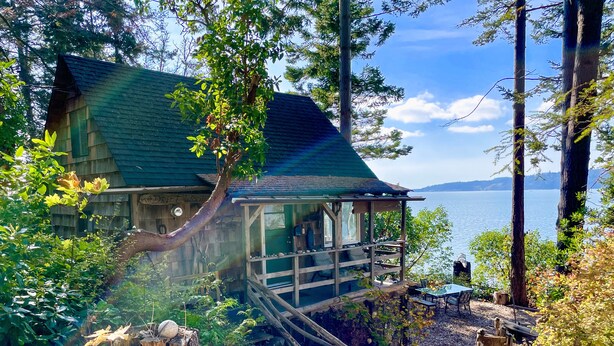 Un chalet rustique doté d’une véranda donnant sur un lac, entouré d’une forêt dense.