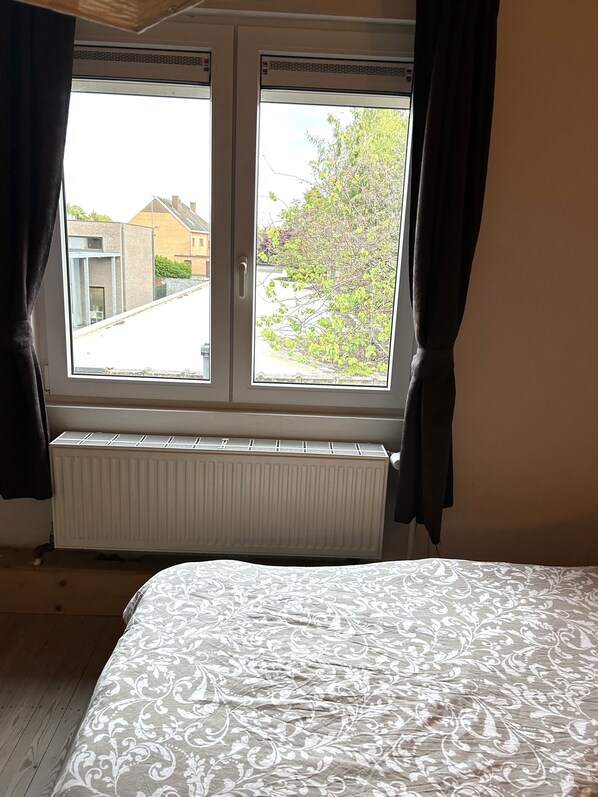 Une chambre avec une fenêtre, un radiateur et un lit recouvert d’une couvre-lit à motifs.