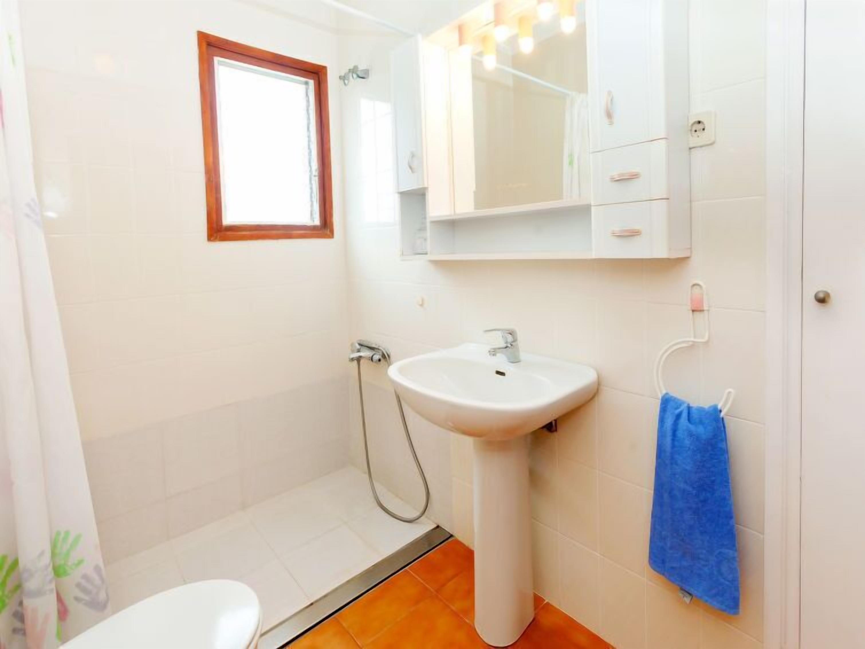 A bathroom with a white sink, a mirror, a window, and a blue towel hanging on the wall.
