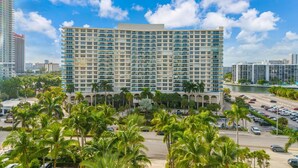 A large, multi-story hotel with a modern design, featuring a prominent central atrium and a parking area with palm trees in the foreground. - Tides Miami 1BR +den Condo on the beach (Hollywood)
