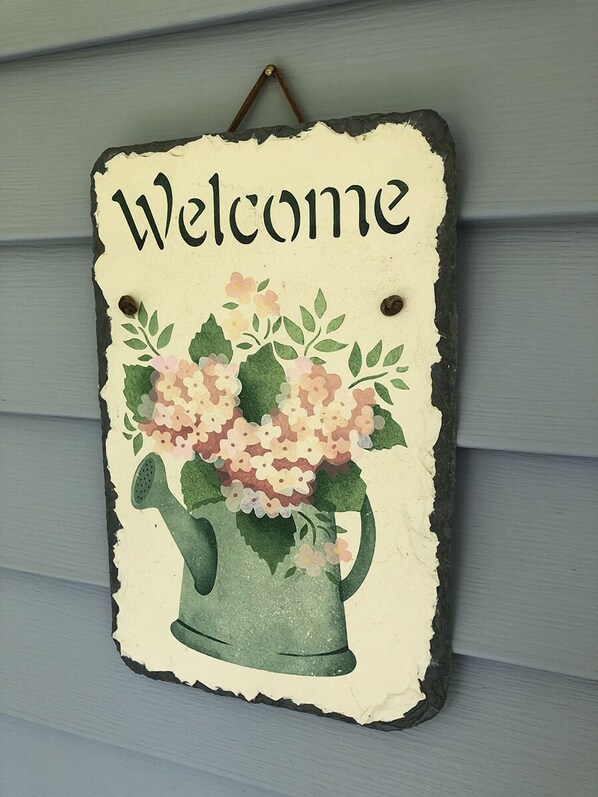 En välkomstskylt med ett blommönster och en vattenkanna.