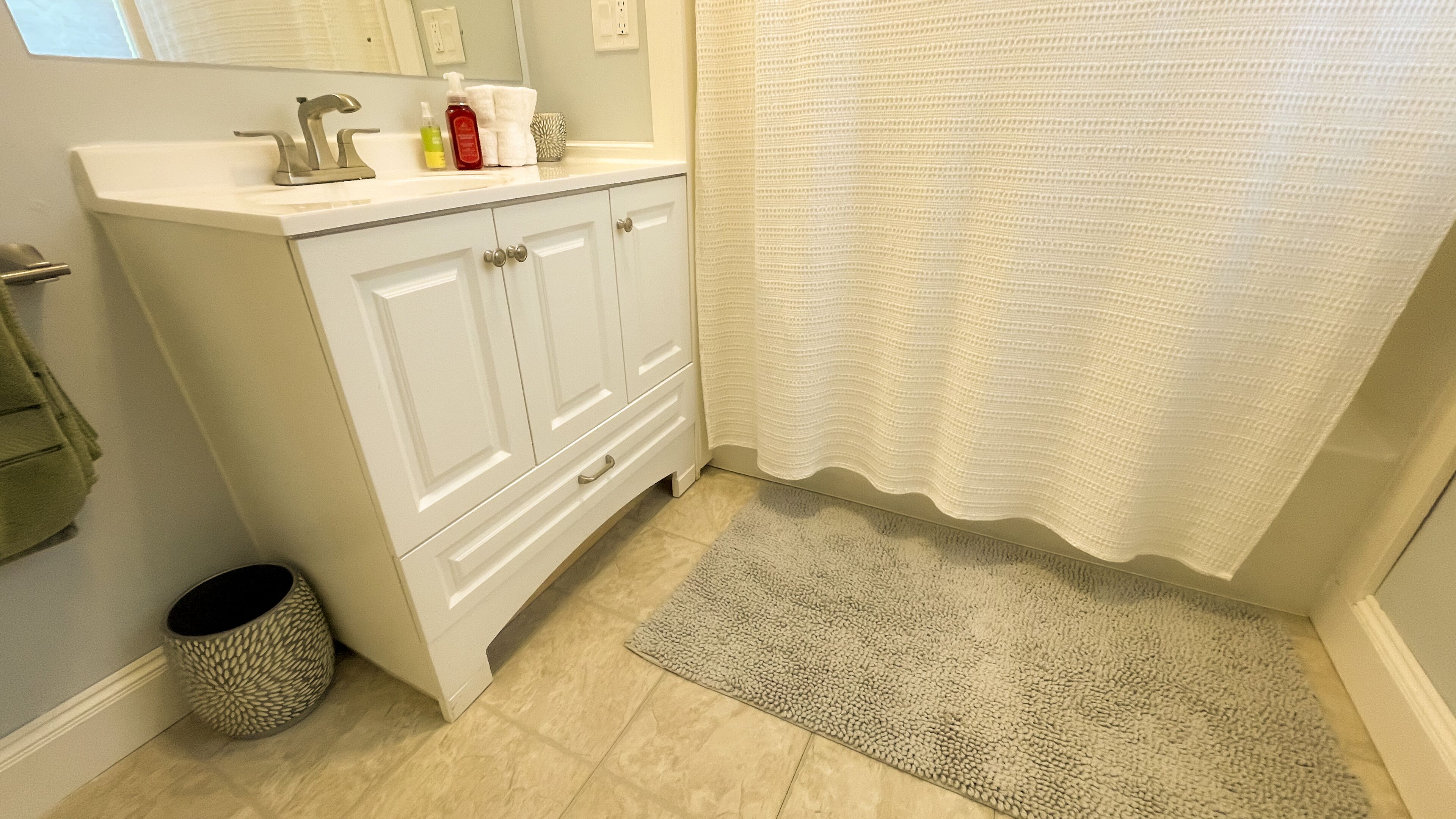 Un baño con tocador blanco, cortina de ducha y alfombra texturizada.