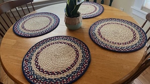 Een ronde houten tafel met vier gevlochten placemats met een rood, wit en blauw patroon.