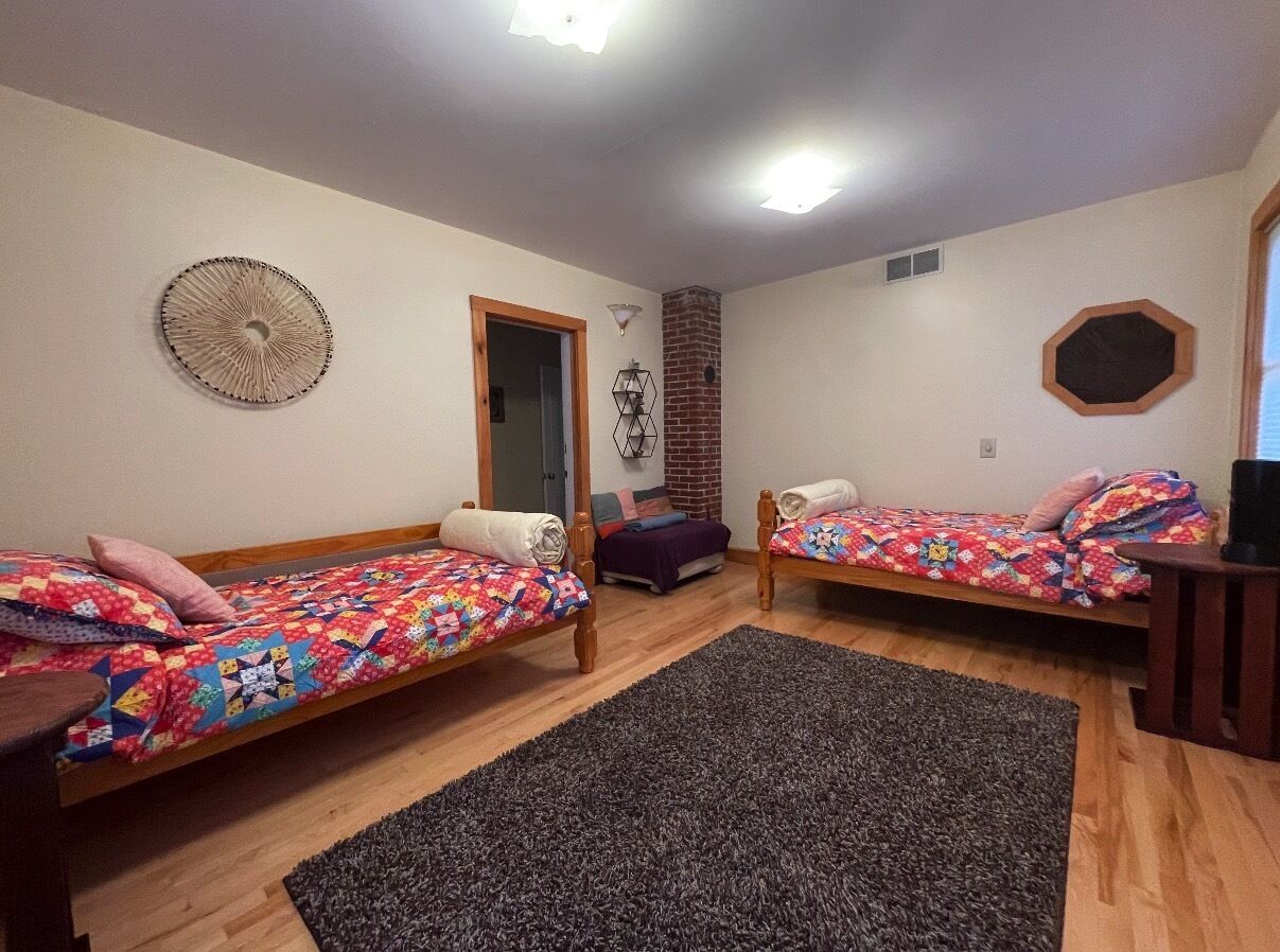 A bedroom with two wooden beds, a brick wall, a fan, and a small table.