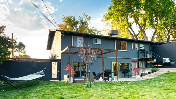 Une maison moderne à deux étages, dotée d’un patio couvert, d’un hamac et d’une pelouse bien entretenue.