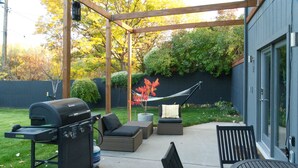 Un jardin avec un barbecue, un coin salon extérieur et un hamac.
