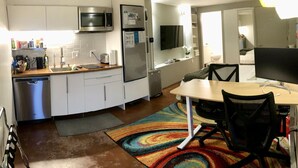 Une cuisine compacte équipée d’un four à micro-ondes, d’un réfrigérateur et d’un évier. On y trouve une table à manger avec des chaises et un tapis coloré.