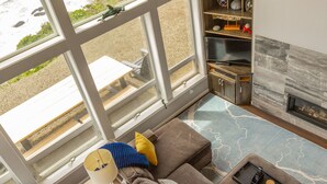 A living room with a large window overlooking the beach, a fireplace, and a cozy seating area. - Lookout House - Romantic Luxury and Ocean Views (Gold Beach)