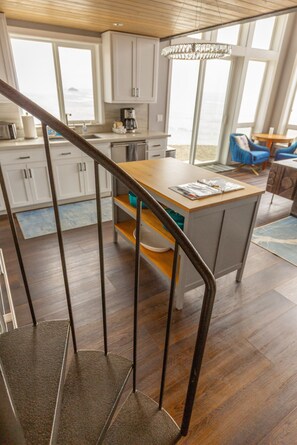 A modern kitchen with a wooden staircase, large windows, and a view of the sea. - Lookout House - Romantic Luxury and Ocean Views (Gold Beach)