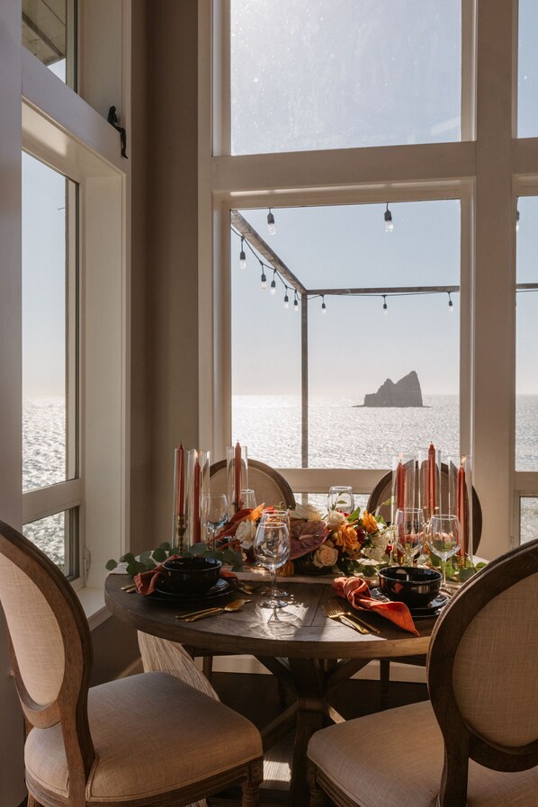A dining table set for two with candles, glasses, and a view of the sea.