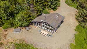 An aerial view of a cabin with a large deck, surrounded by dense forest. - Lookout House - Romantic Luxury and Ocean Views (Gold Beach)