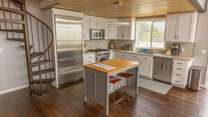 A modern kitchen with a central island, stainless steel appliances, and a wooden ceiling. - Lookout House - Romantic Luxury and Ocean Views (Gold Beach)