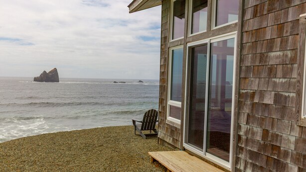 A wooden building with a large glass door and windows overlooking the ocean. - Lookout House - Romantic Luxury and Ocean Views (Gold Beach)