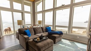 A spacious living room with a large sectional sofa, a coffee table, and a view of the ocean through large windows. - Lookout House - Romantic Luxury and Ocean Views (Gold Beach)