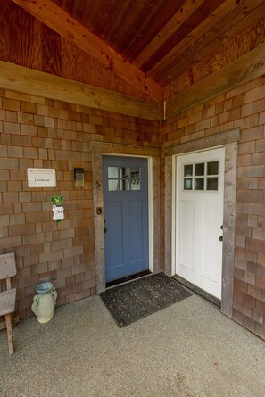 A wooden building entrance with a blue door, a white door, a lookout sign, and a ceramic pot. - Lookout House - Romantic Luxury and Ocean Views (Gold Beach)