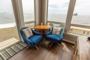 A room with two blue armchairs, a wooden table, and a view of the ocean.