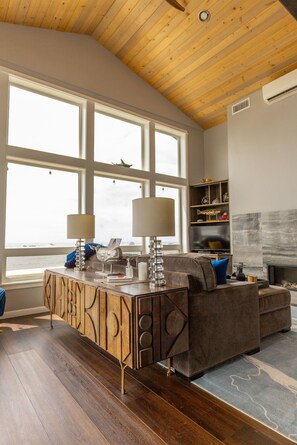 A modern living room with a wooden ceiling, large windows, a fireplace, and a built-in entertainment unit.