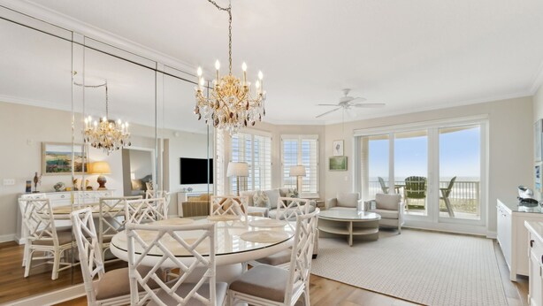 A spacious living area with a round glass table, white wicker chairs, a chandelier, and a view of the outdoors through large sliding glass doors. - 81 Ocean Place - Lovely Oceanfront 3rd Floor With Views Of The Atlantic Ocean (Fernandina Beach)